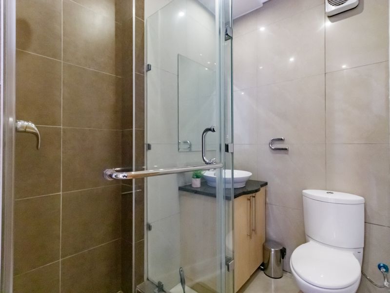 Modern bathroom featuring a glass-enclosed shower, vanity cabinet with vessel sink, and a standard toilet with neutral wall tiling.