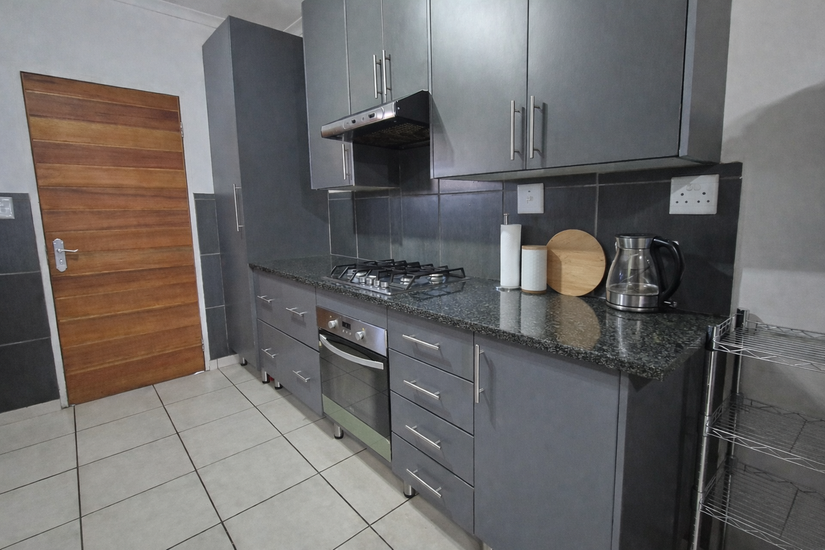 Modern kitchen featuring dark grey cabinetry, granite countertops, a gas hob, built-in oven, and tiled flooring with a solid wood door.
