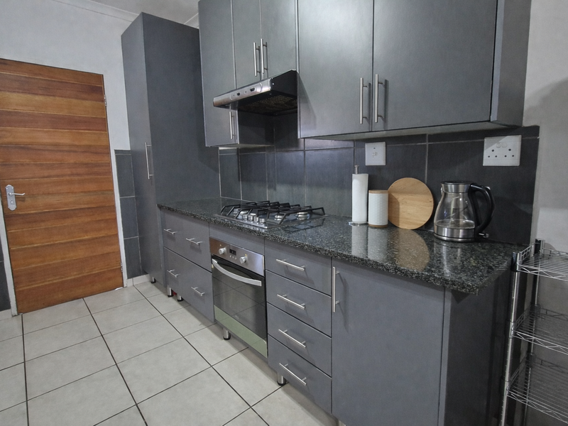 Modern kitchen featuring dark grey cabinetry, granite countertops, a gas hob, built-in oven, and tiled flooring with a solid wood door.