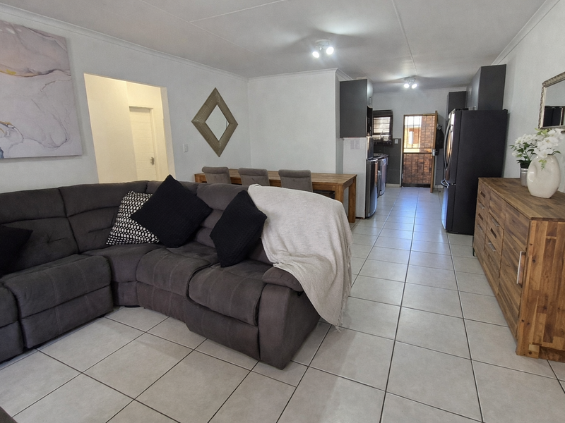 An open-plan living and dining area featuring neutral tiled flooring, modern kitchen cabinetry, and a seamless flow between the lounge and kitchen spaces.