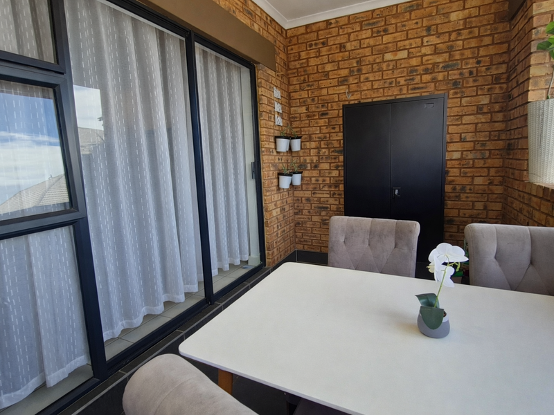 A covered patio area featuring exposed brick walls, tiled flooring, and large sliding glass doors providing seamless access to the interior living space.