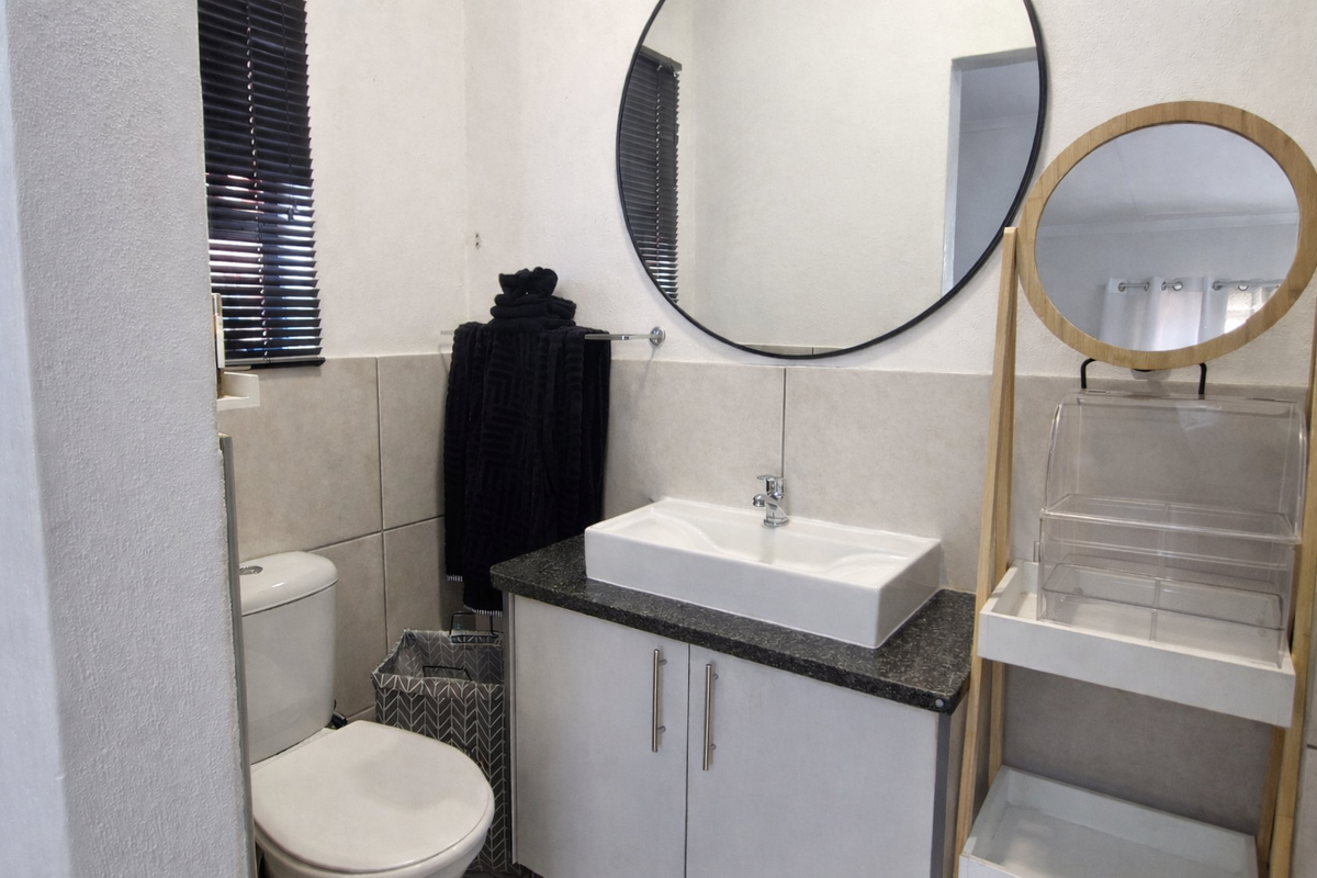 A modern bathroom featuring a vessel sink on a granite countertop, vanity cabinet, toilet, and a large circular wall-mounted mirror.