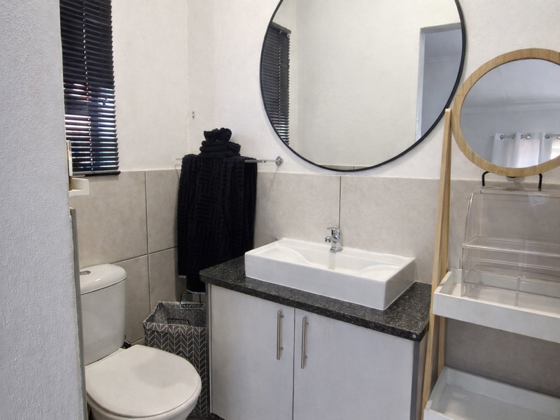 A modern bathroom featuring a vessel sink on a granite countertop, vanity cabinet, toilet, and a large circular wall-mounted mirror.