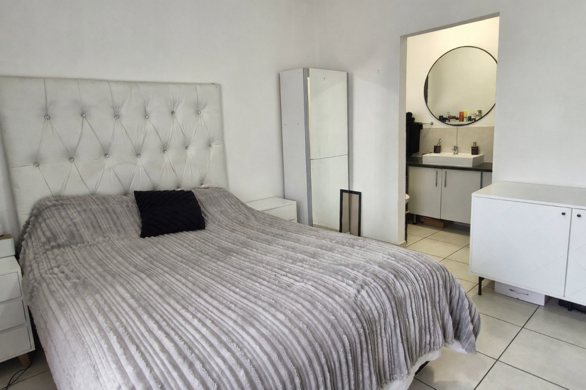 A bedroom featuring tiled flooring and an open-plan en-suite bathroom with a vanity cabinet, basin, and wall mirror.