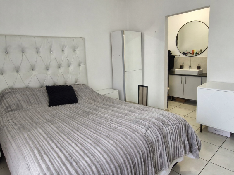 A bedroom featuring tiled flooring and an open-plan en-suite bathroom with a vanity cabinet, basin, and wall mirror.