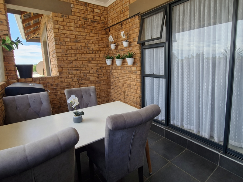 A covered balcony featuring exposed brick walls, dark floor tiles, and large sliding glass doors providing access to the interior.