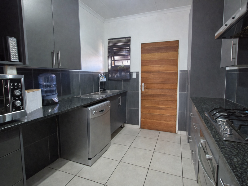 Modern kitchen featuring dark grey cabinetry, granite countertops, stainless steel gas hob, oven, extractor fan, and tiled finishes throughout.