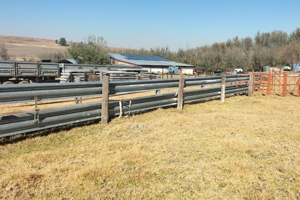 A view of the farm grounds featuring metal guardrail fencing, open grazing land, and agricultural outbuildings in the background.