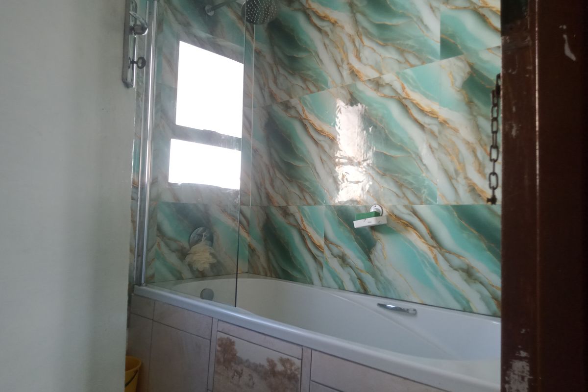 A bathroom featuring a bathtub with a glass shower screen and decorative marble-effect wall tiling.