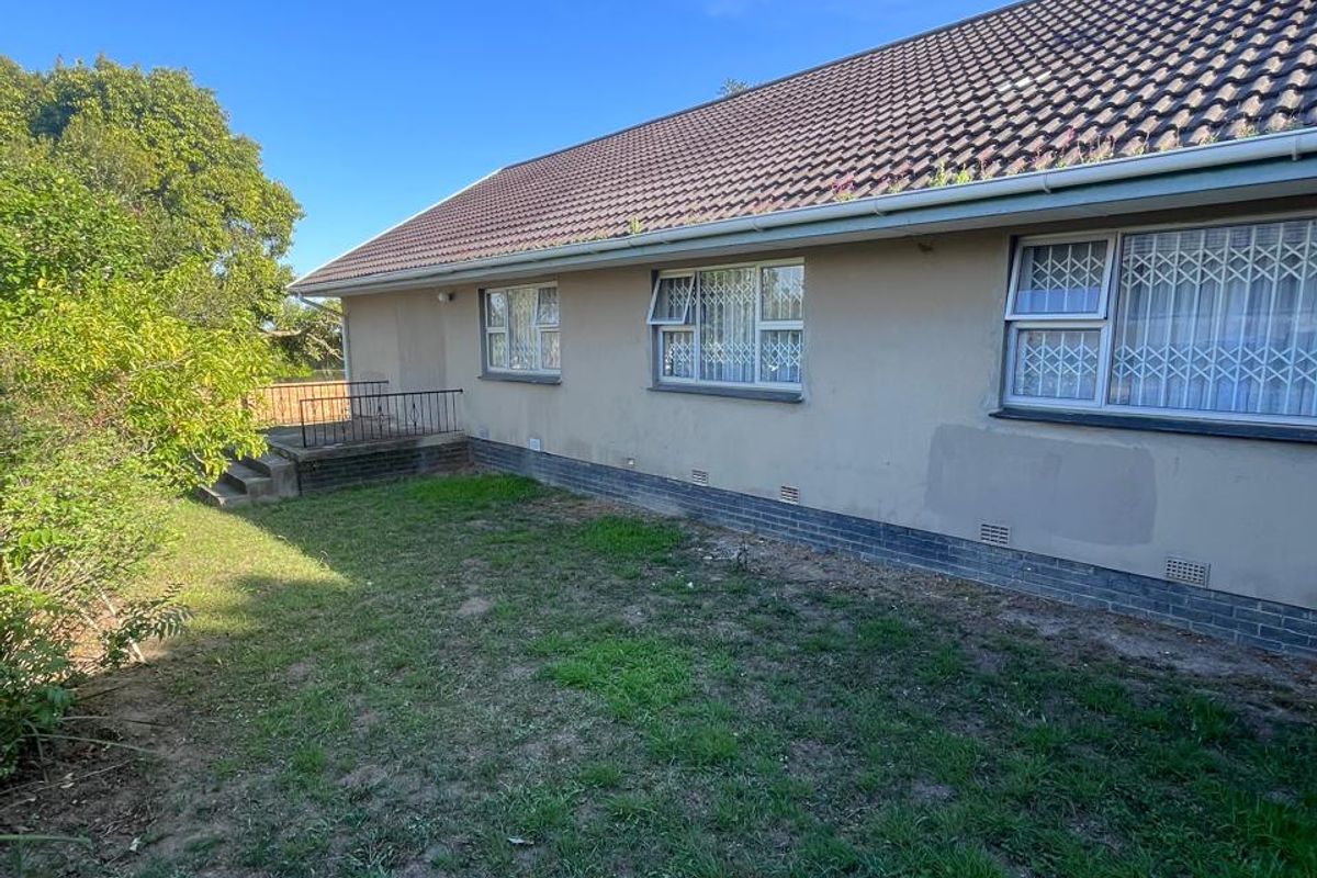 Rear exterior view of the house featuring a tiled roof, security bars on windows, and a small concrete patio area leading to the garden.
