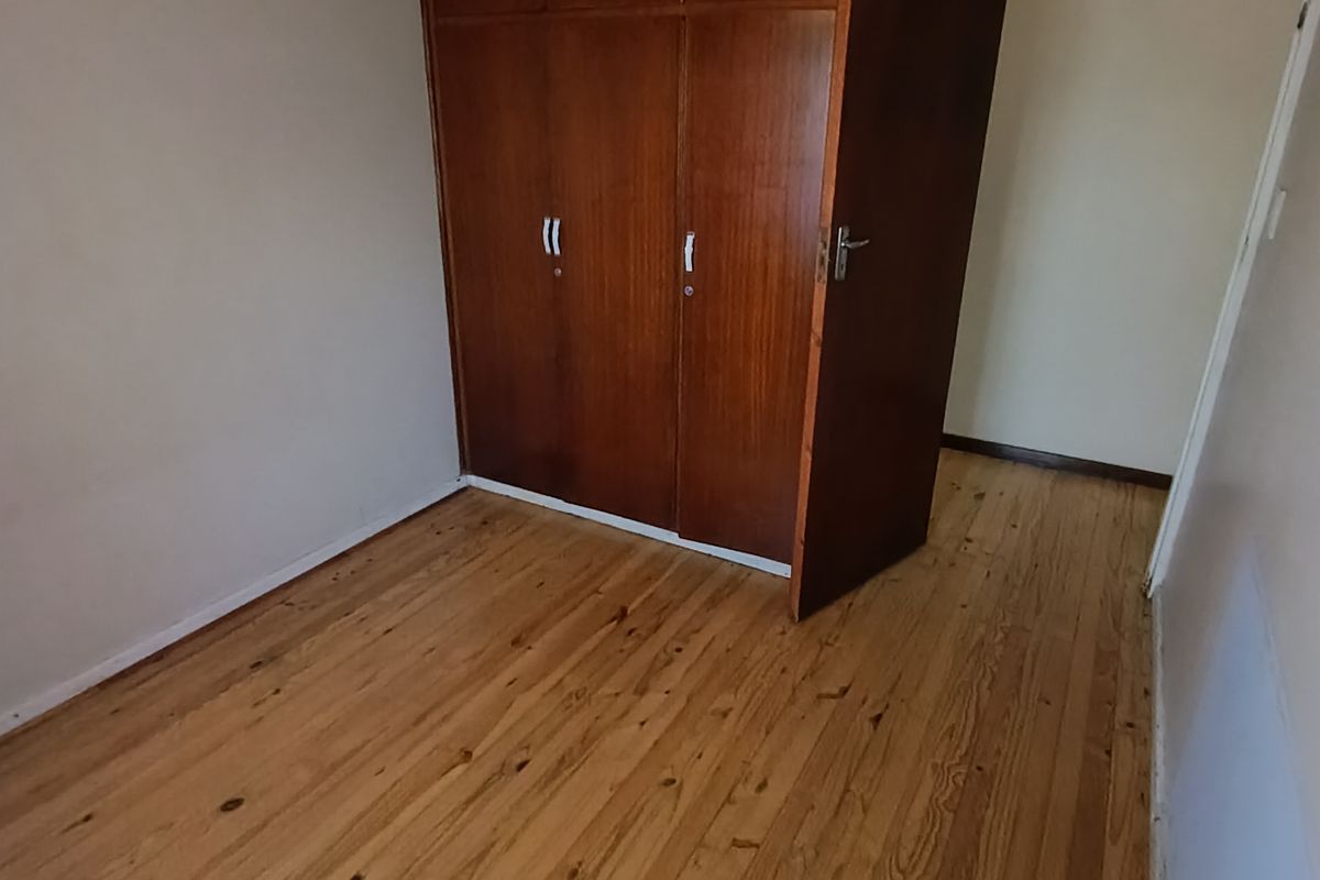 A bedroom featuring polished wooden flooring and built-in wooden cabinetry, offering a clean and functional space.