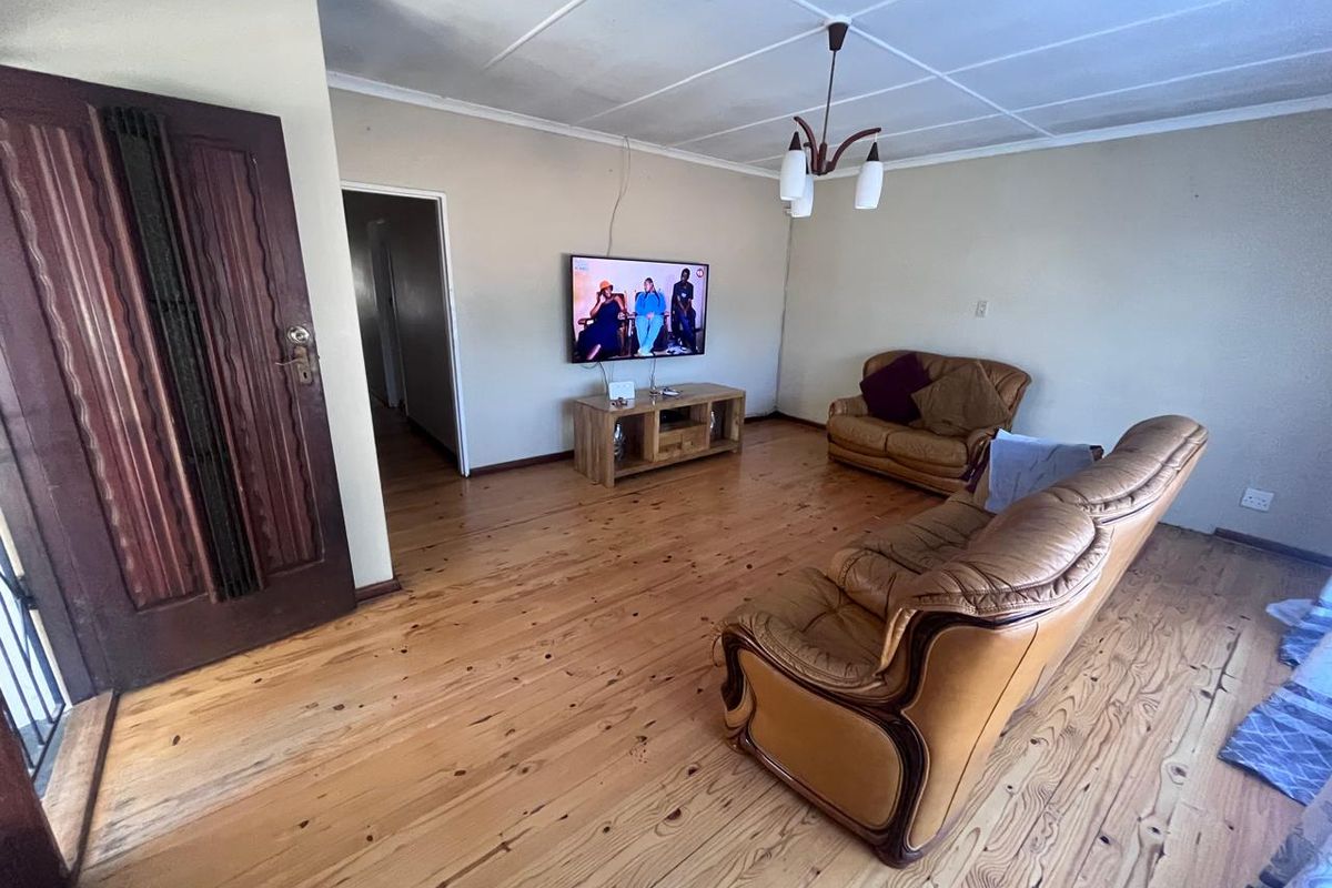 A living room featuring polished timber flooring, a ceiling-mounted light fixture, and a solid timber entrance door.