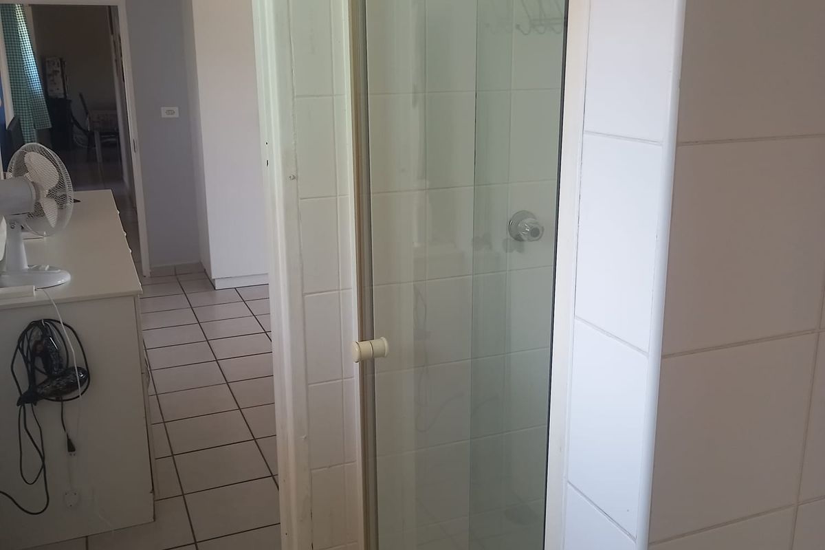 A functional bathroom featuring a shower enclosure with tiled walls and flooring, showing signs of age and wear.
