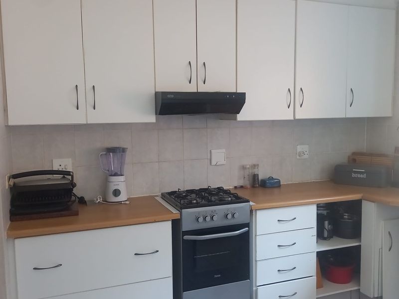 A functional kitchen featuring white cabinetry, a gas stove with extractor fan, tiled backsplash, and laminate countertops, offering a practical layout for daily cooking.