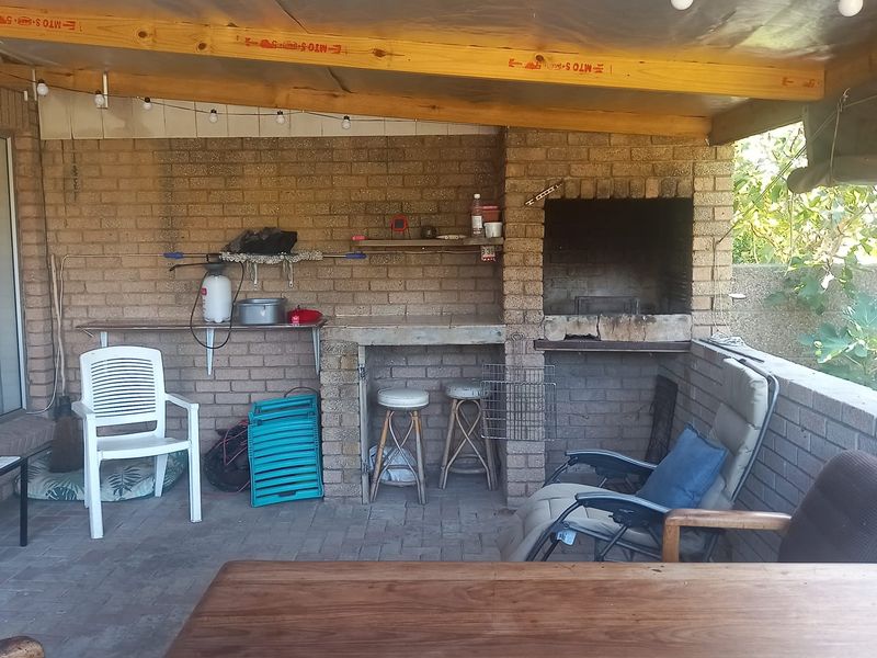 Covered outdoor patio area featuring a built-in brick braai, concrete prep surface, and timber beam ceiling, ideal for outdoor entertaining.