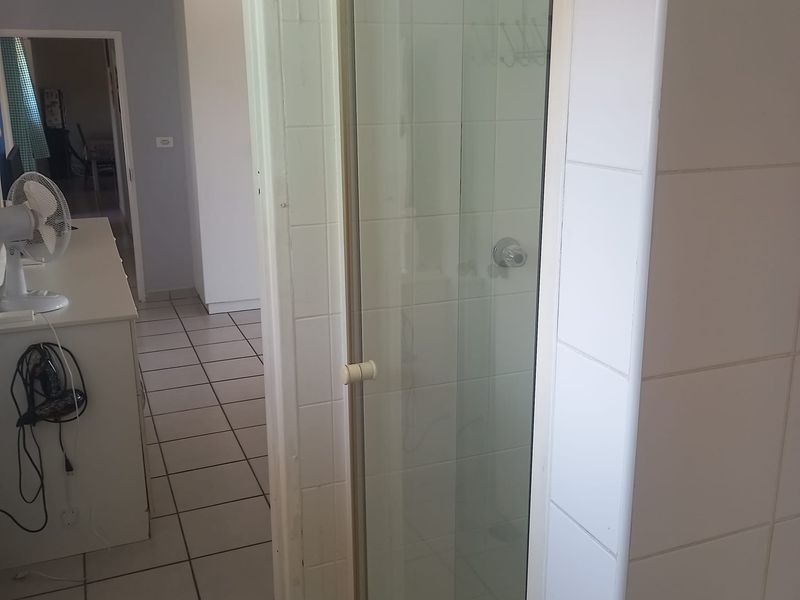 A functional bathroom featuring a shower enclosure with tiled walls and flooring, showing signs of age and wear.