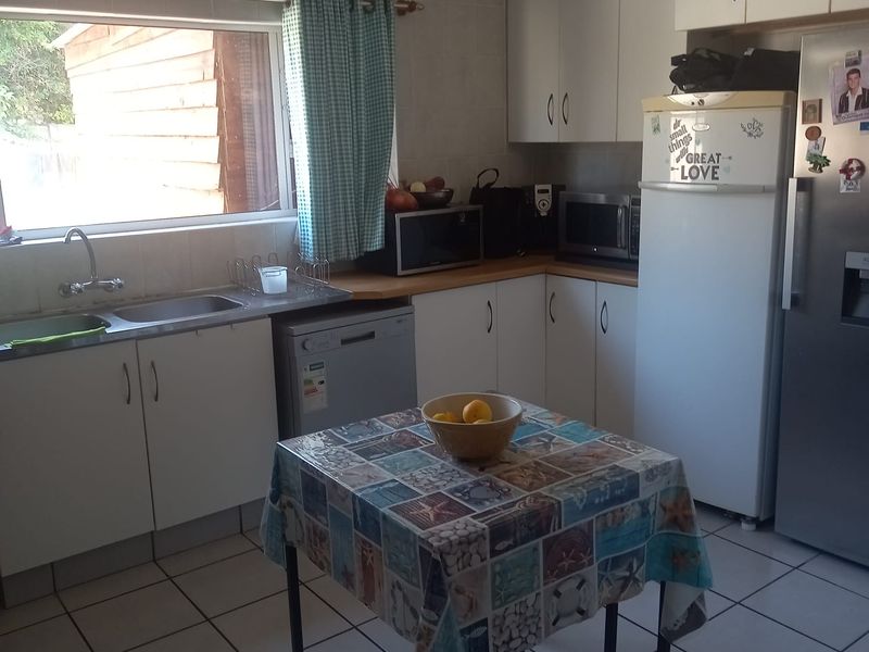 A functional kitchen featuring white cabinetry, tiled splashbacks, tiled flooring, and a double basin sink with natural light from the window.