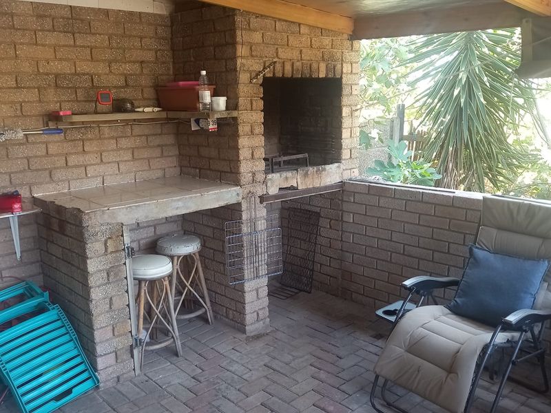 Covered outdoor patio area featuring a built-in brick braai, tiled prep counter, and brick paved flooring, ideal for outdoor entertaining.