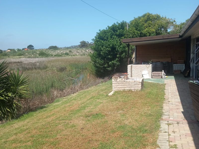 Rear exterior view featuring a paved patio, built-in brick braai, and a lawn area overlooking natural wetlands.