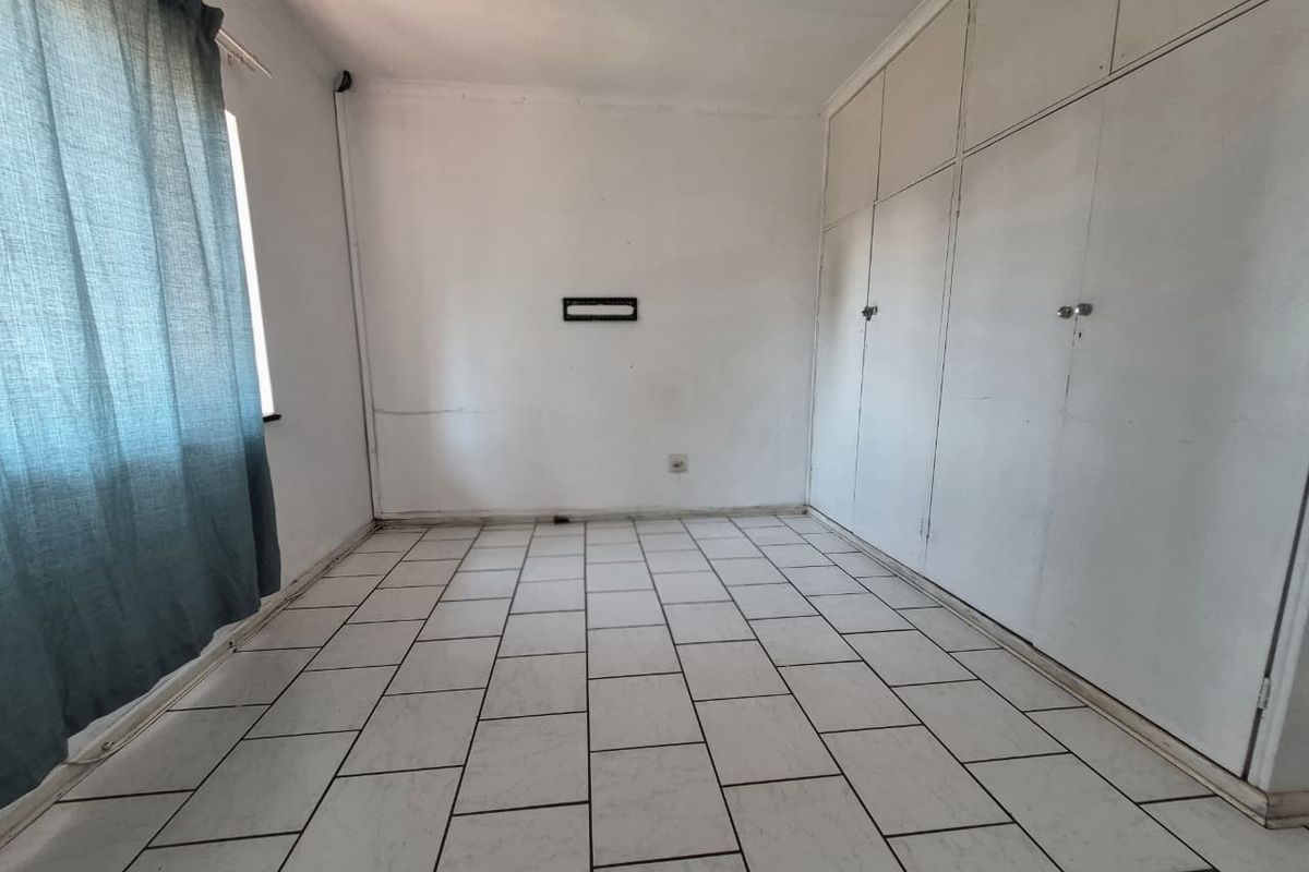 An empty bedroom featuring tiled flooring, built-in cupboards, and a ceiling fan, requiring some cosmetic updates to the wall finishes.