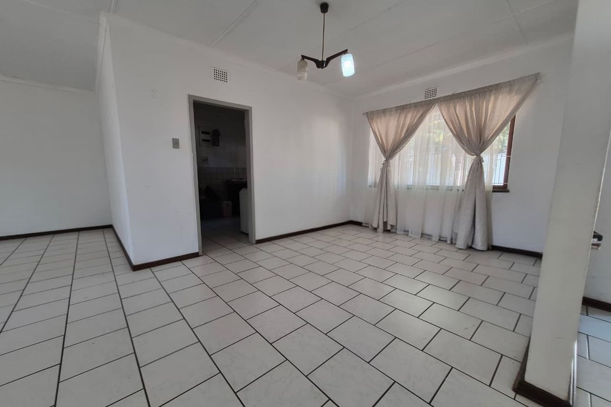 An empty living room featuring ceramic floor tiles, a central light fixture, and a window with curtain tracks, offering a blank canvas for renovation.