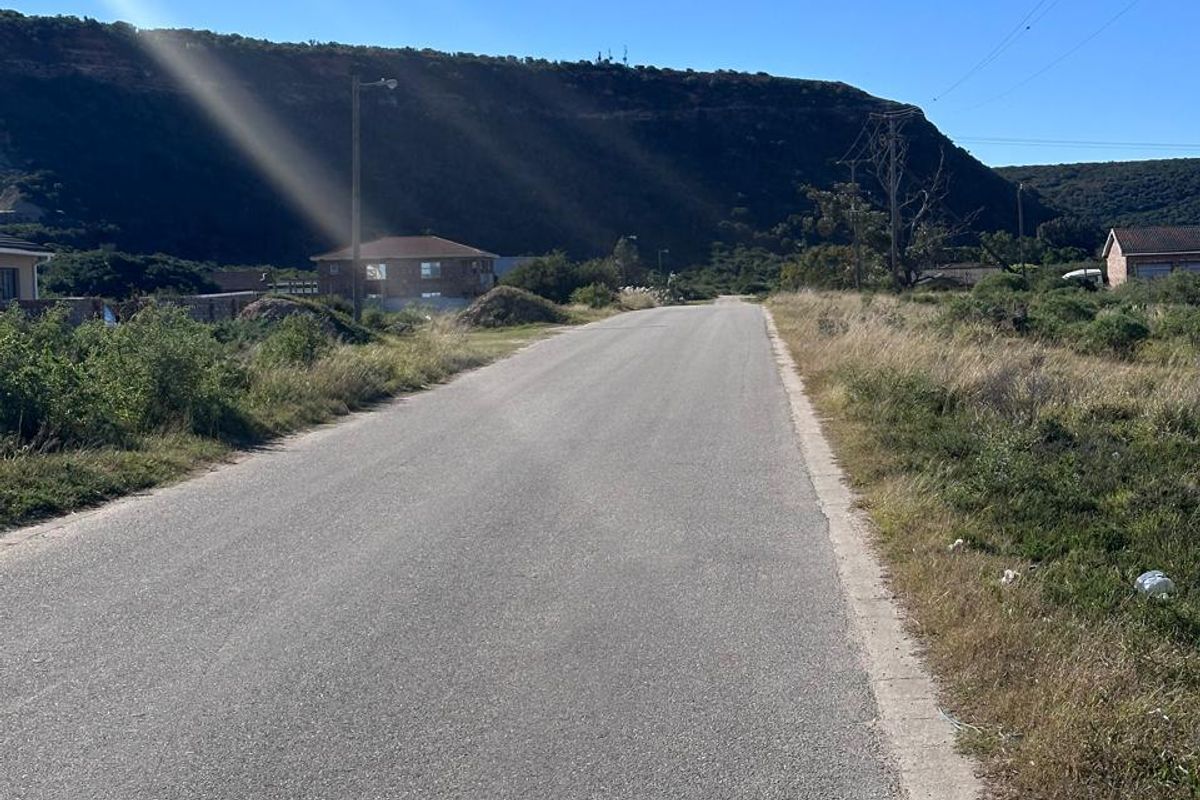 A view of the paved street leading through the residential area, featuring surrounding natural landscape and distant hills.