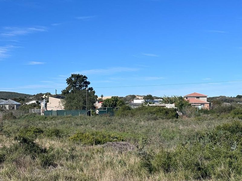 A view of a vacant residential plot featuring natural vegetation and surrounding neighborhood homes in the distance.