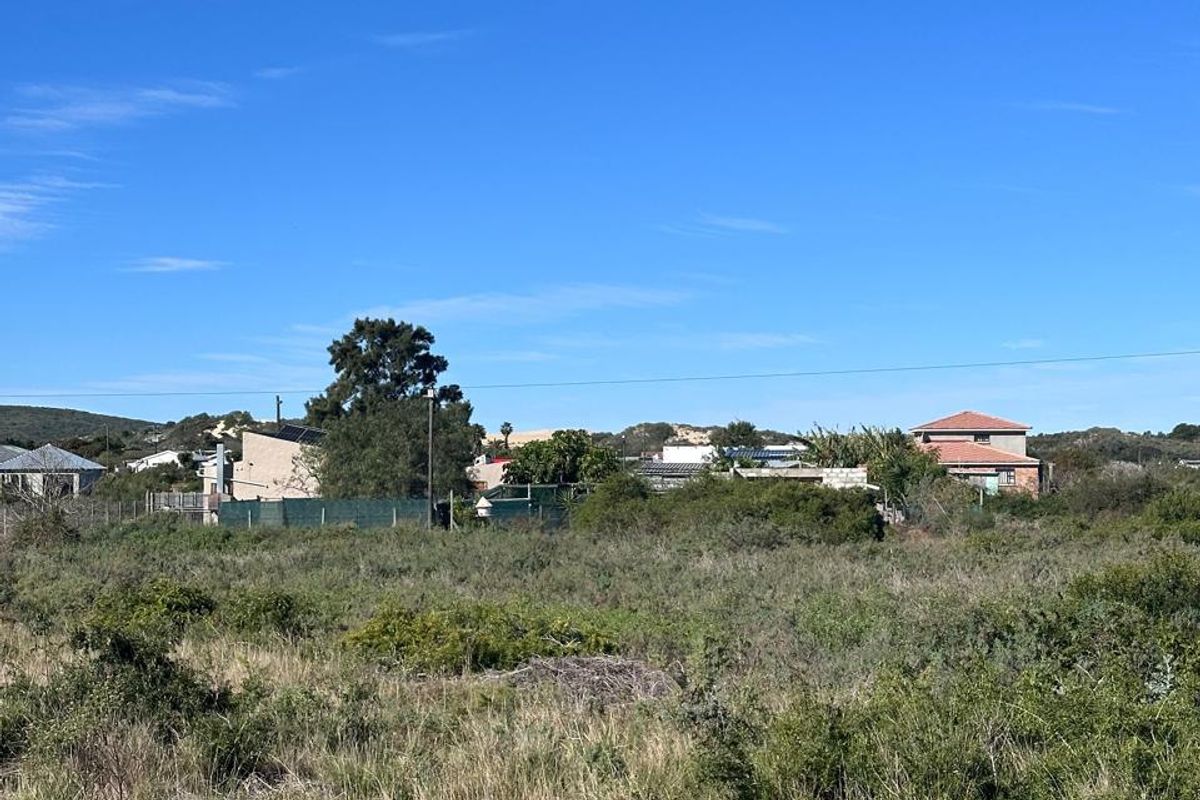 A view of a vacant residential plot featuring natural vegetation and surrounding neighborhood homes in the distance.