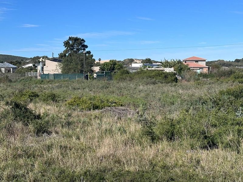 A vacant residential plot covered in natural vegetation, offering a clear view of the surrounding neighborhood and established residential properties.