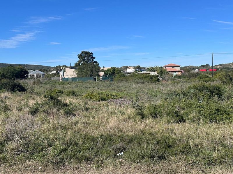 A view of a vacant residential plot featuring natural vegetation and surrounding neighborhood homes in the distance.