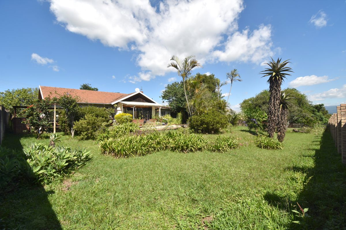 A spacious rear garden featuring a well-maintained lawn, mature landscaping, and a covered patio area attached to the main house structure.