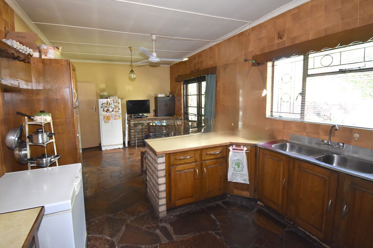 A dated kitchen featuring wooden cabinetry, stone flooring, and tiled walls, offering a functional layout with potential for modern renovation.