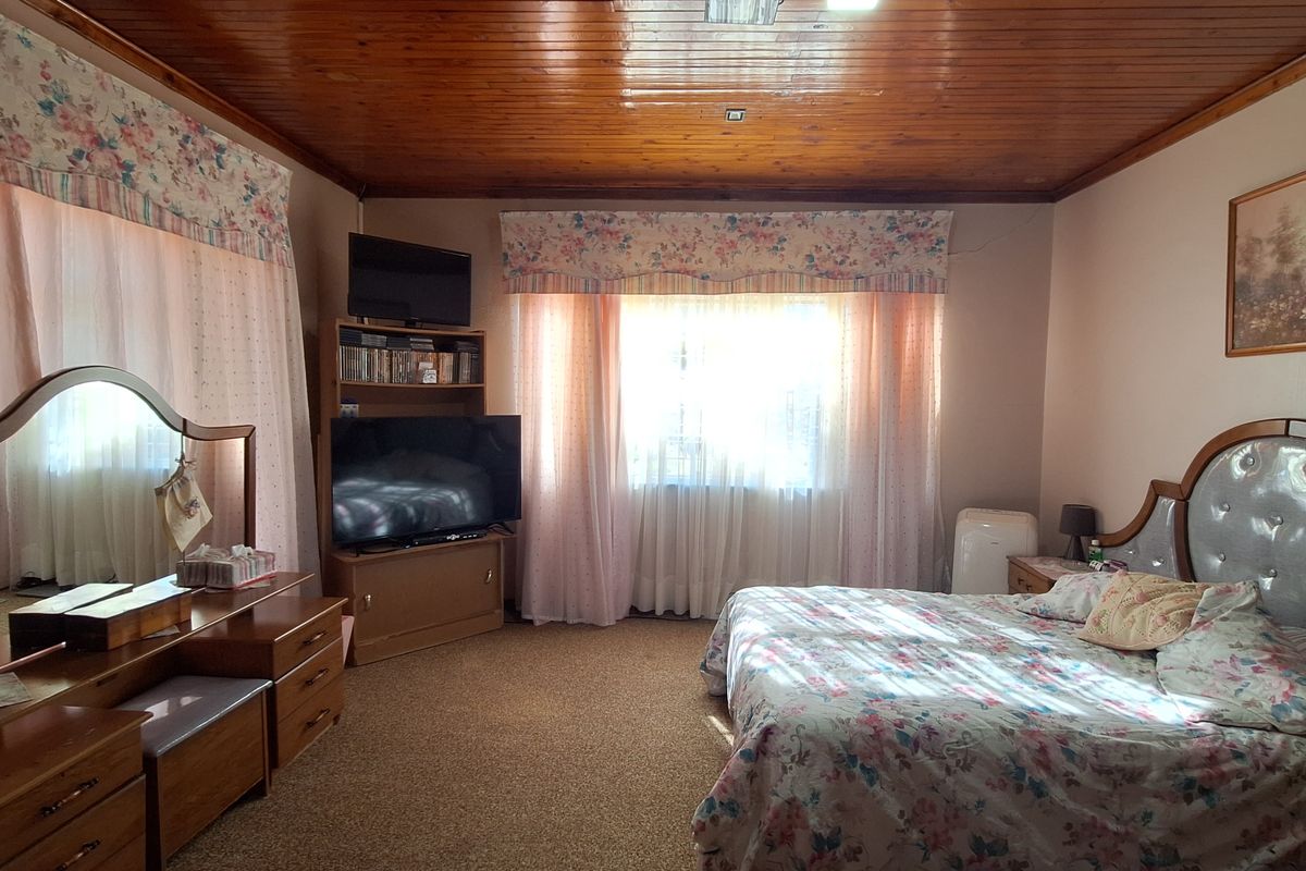 Spacious bedroom featuring a traditional wood-paneled ceiling, carpeted flooring, and large windows with natural light.