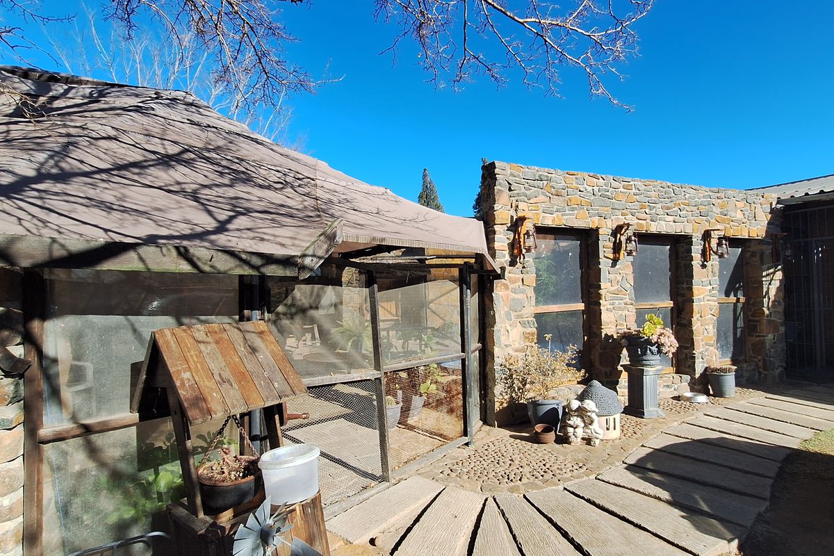 Outdoor area featuring a stone-clad wall, a covered enclosure with wire mesh, and a paved stone walkway in a rustic farm setting.