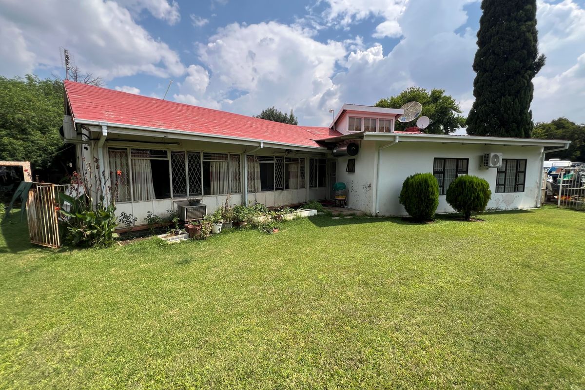 Rear view of a single-story house featuring a red metal roof, white exterior walls, and a spacious lawn area.