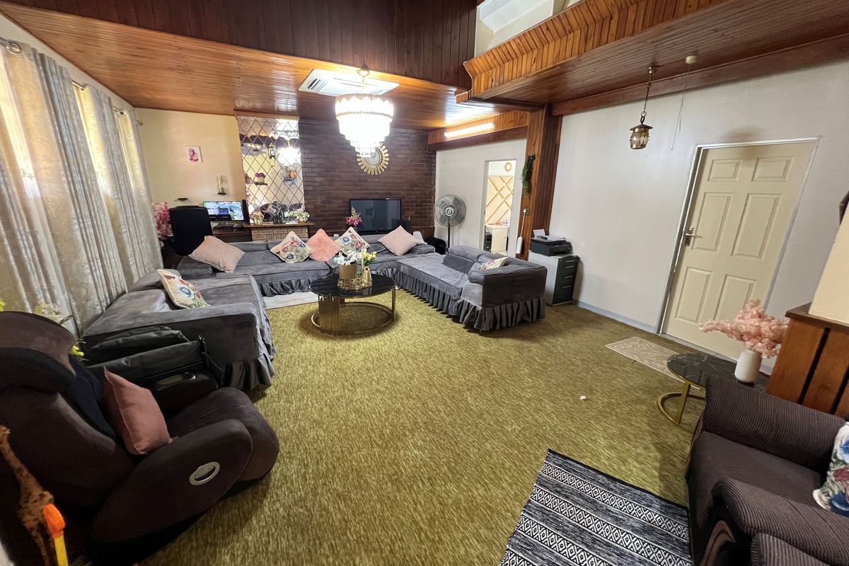 Spacious living room featuring a high timber-clad vaulted ceiling, a brick feature wall, and a central chandelier, offering a dated but functional layout.