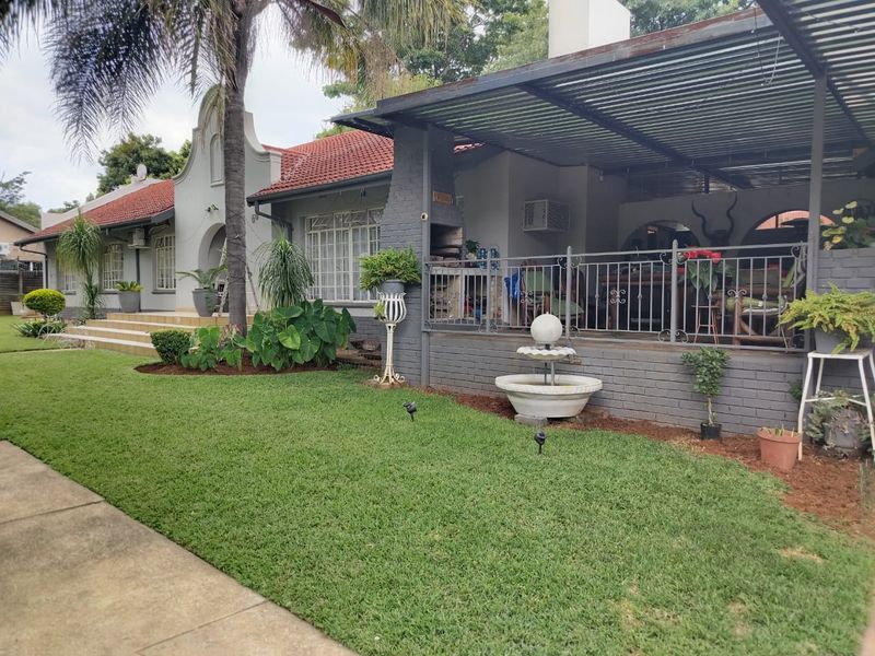 A well-maintained rear garden featuring a covered patio with a built-in braai, brick masonry, and a decorative water fountain.