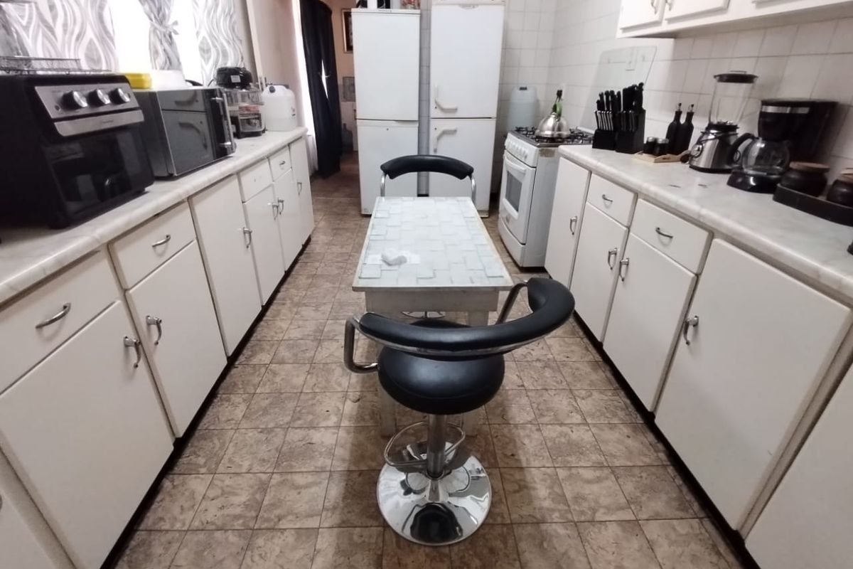 A functional galley-style kitchen featuring white cabinetry, tiled countertops, and a central breakfast bar area with tiled flooring.