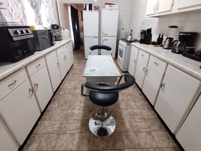 A functional galley-style kitchen featuring white cabinetry, tiled countertops, and a central breakfast bar area with tiled flooring.