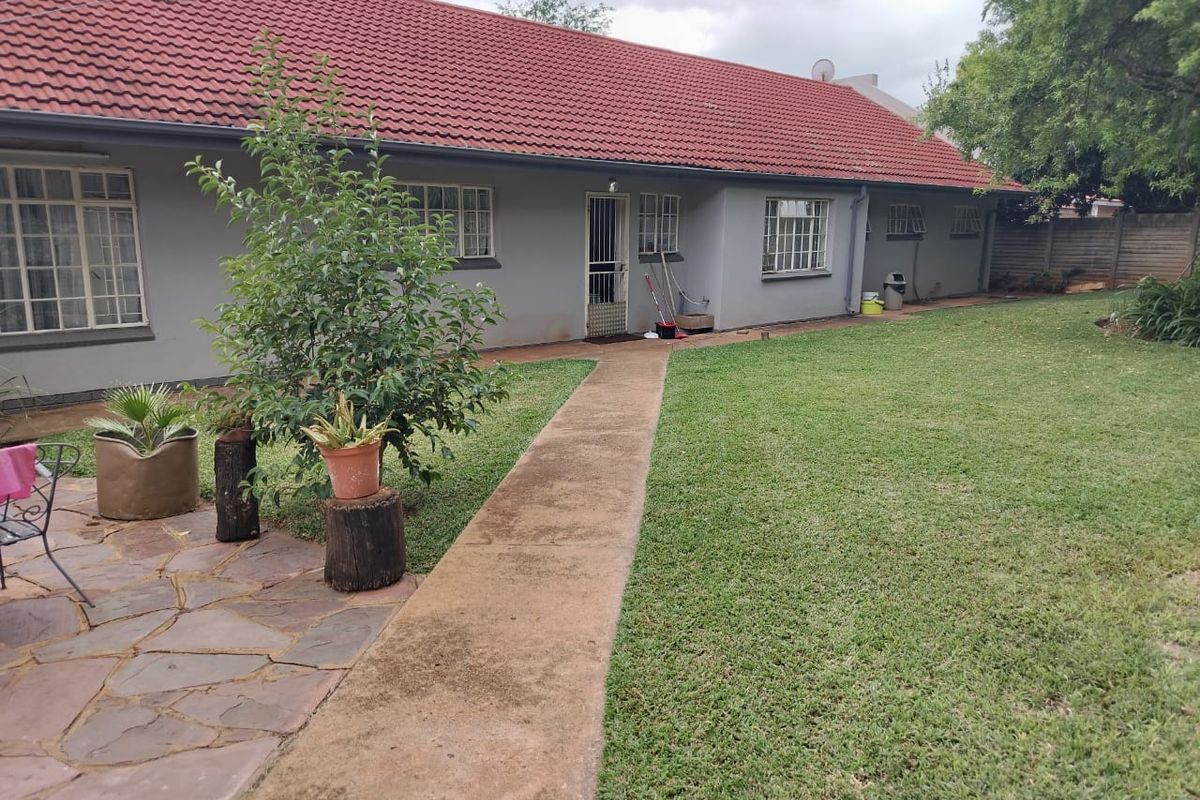 Rear view of the house featuring a red tiled roof, grey exterior walls, a concrete pathway, and a spacious lawn area.