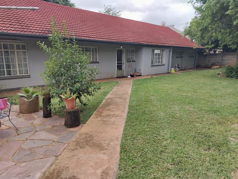 Rear view of the house featuring a red tiled roof, grey exterior walls, a concrete pathway, and a spacious lawn area.