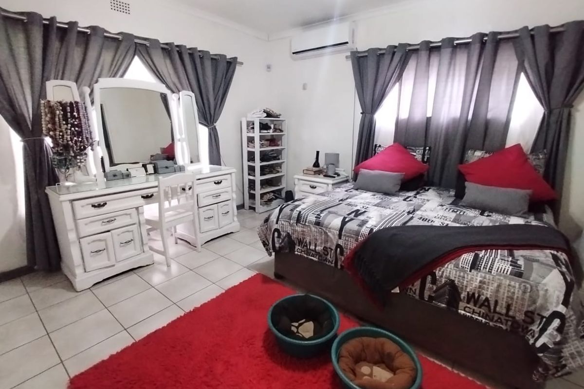 A bedroom featuring tiled flooring, a wall-mounted air conditioning unit, and dual window treatments.