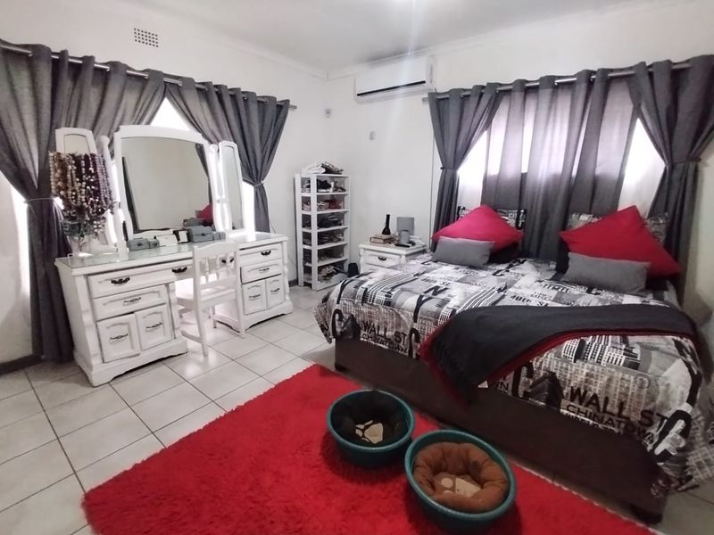 A bedroom featuring tiled flooring, a wall-mounted air conditioning unit, and dual window treatments.