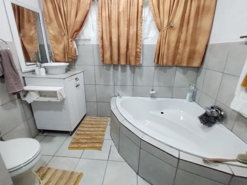 A functional bathroom featuring a corner bathtub, tiled walls, and a vanity basin unit.