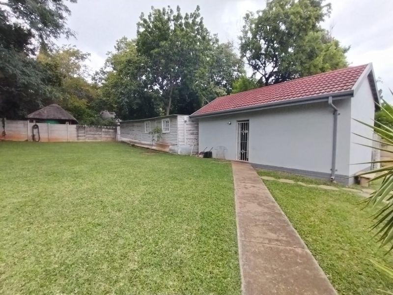 A view of the rear garden featuring a lawn, a concrete pathway, and a detached outbuilding with a tiled roof.