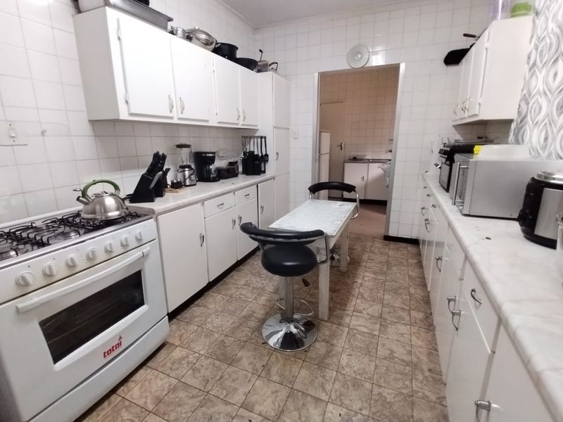A functional kitchen featuring white cabinetry, tiled walls, and a gas stove, with an adjacent scullery area visible through the doorway.