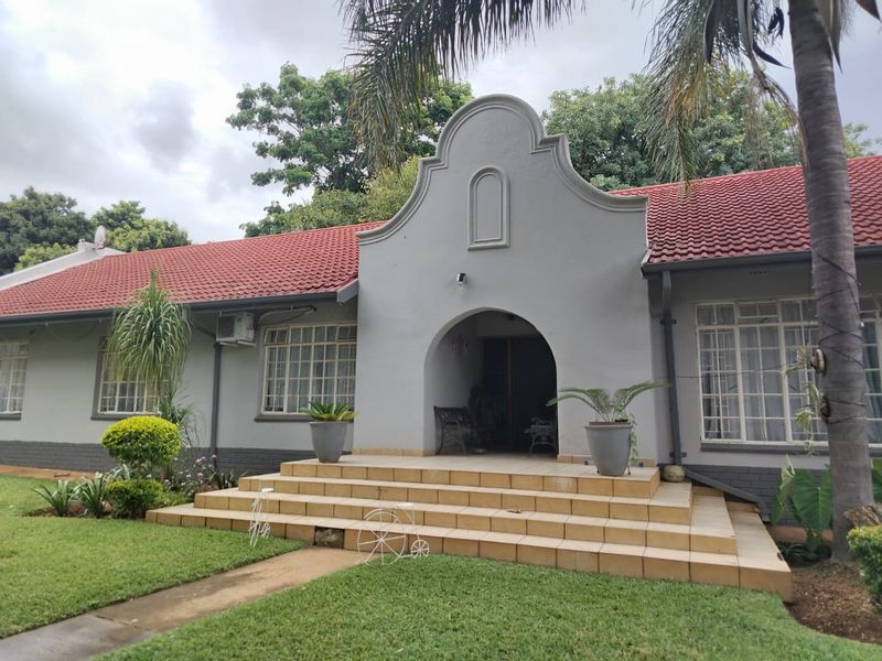 Front elevation of a traditional house featuring a distinctive arched entrance, tiled steps, and a red pitched roof set within a landscaped garden.