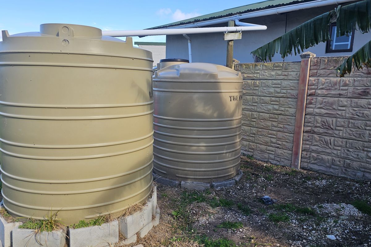 Rear yard area featuring two large plastic water storage tanks positioned against a precast concrete boundary wall with connected guttering infrastructure.
