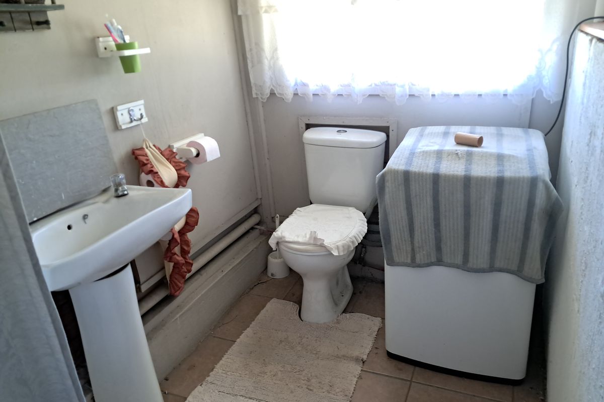 A compact bathroom featuring a pedestal basin and toilet with tiled flooring, offering potential for modernization and cosmetic updates.