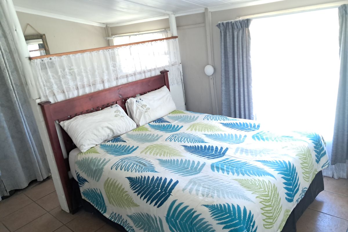 A bedroom featuring tiled flooring and a timber-paneled ceiling, with a partition wall separating the sleeping area.